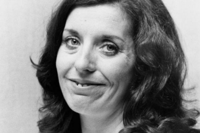 Schwarzweiß-Porträt: lächelnde Frau mit schulterlangen, gewellten dunklen Haaren, Blick zur Kamera.